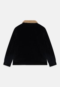 Chaqueta de pana negra con cuello de borreguillo beige, mangas largas y puños botones, mostrada desde la parte de atrás sobre un fondo blanco.
