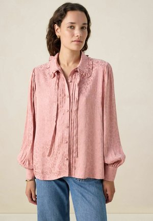 Blouse en soie rose avec un col volanté, un devant boutonné et des détails plissés, avec de longues manches resserrées aux poignets. Motif léopard subtil.