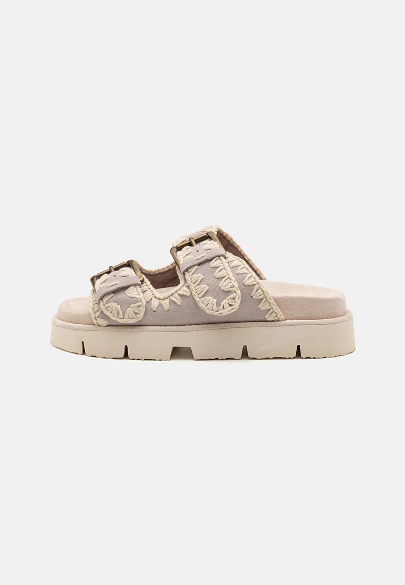 Suede slide sandal in light beige with decorative stitching, adjustable buckles, and a thick, textured sole for added grip and support.