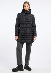 Zwarte pufferjas met capuchon, voorzien van horizontale stiksels, knopen aan de voorkant en zijzakken; gedragen met grijze jeans en zwarte laarzen.