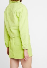Conjunto de chaqueta y pantalones cortos de mezclilla verde lima, con un diseño ajustado, cuello, bolsillo en el pecho y cierre de presión. Textura suave con una tela ligera.