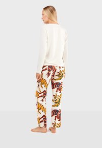 Lange mouw crèmekleurig top gecombineerd met gestreepte broek met meerkleurige tijgers op een witte achtergrond. Casual, relaxte pasvorm.