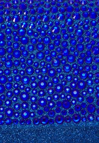 Blå glittrig yta tätt täckt med olika storlekar av glittrande, runda blåa rhinstenar som är ordnade nära varandra.