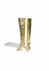 Čizme od zlatne metalik boje do koljena, s šiljastim vrhom i potpeticom na stiletto. Imaju glatku, sjajnu teksturu i elegantan dizajn.