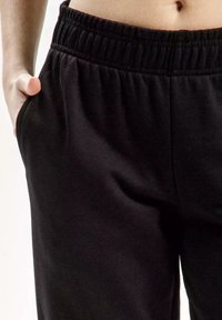 Czarne dresy z elastycznym pasem, posiadające boczne kieszenie oraz gładką, teksturowaną tkaninę, która wygodnie układa się na ciele.