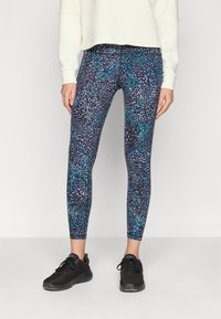 Rugalmas anyagból készült leggings, sötétkék alapon színes pettyes mintával. Fekete sportcipővel párosítva.