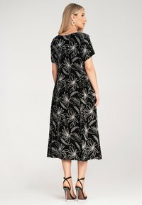 Black dress with short sleeves, featuring a white floral pattern. Flowy design, knee-length, paired with black strappy heels. Smooth texture.