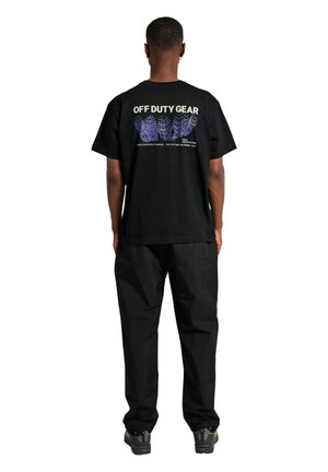 Man draagt een zwart T-shirt met de tekst "OFF DUTY GEAR" en blauwe bandenspoorgrafieken op de achterkant, gecombineerd met een zwarte broek en sneakers, met de rug naar de kijker.