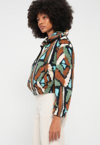 Fleecová bunda so zapínaním na zips s geometrickým vzorom v zemných odtieňoch hnedej, zelenej a modrej. Stojatý golier a elastické manžety.