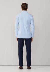 Lichtblauw overhemd met lange mouwen en een button-downkraag, gedragen met marineblauwe broek en bruine schoenen, gezien vanaf de achterkant.