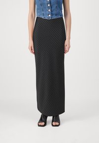 Jupe maxi à pois noir et blanc avec une silhouette ajustée, associée à un crop top en denim et des sandales à talons ouverts noires.