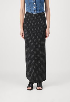 Falda maxi de lunares en blanco y negro con una silueta ajustada, combinada con una camiseta de mezclilla cropped y sandalias de tacón abiertas en negro.