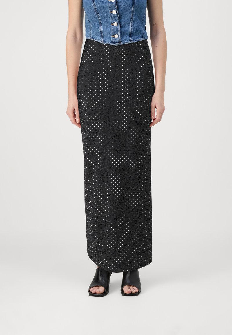 Jupe maxi à pois noir et blanc avec une silhouette ajustée, associée à un crop top en denim et des sandales à talons ouverts noires.