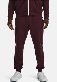 Chándal atlético color burdeos con chaqueta con cremallera y pantalones. Presenta una textura suave, cinturilla elástica y detalles de logotipo en blanco. Calzado blanco.