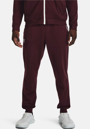 Burgundy träningsdress med zip-up jacka och byxor. Har en mjuk textur, elastisk midjeband och vita logodetaljer. Vita skor.