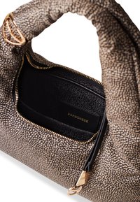 Textured beige and black handbag with a soft, rounded shape, gold hardware accents, and a zippered compartment revealing a black interior.