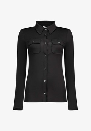 Chemise noire à manches longues avec boutons, col pointu et deux poches à rabats boutonnées à l’avant, présentée sur un fond blanc uni.