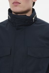 Chaqueta de marina con un alto cuello, dos bolsillos en el pecho y un detalle de cremallera en el cuello. La tela parece suave y resistente al agua.