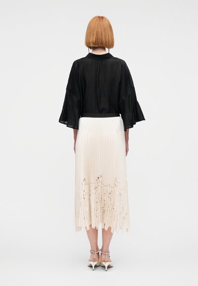 Μαύρο κομμένο μπλουζάκι με φαρδιά μανίκια, συνδυασμένο με κρεμ πλισέ φούστα με δαντελένια λεπτομέρεια στο τελείωμα. Η κομψή υπόδηση ολοκληρώνει την εμφάνιση.