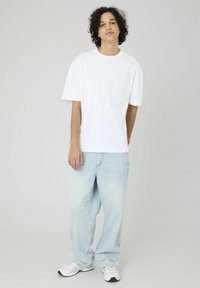 T-shirt blanche à manches courtes avec une poche, associé à un jean bleu clair ample et des baskets blanches. Tenue simple et décontractée.