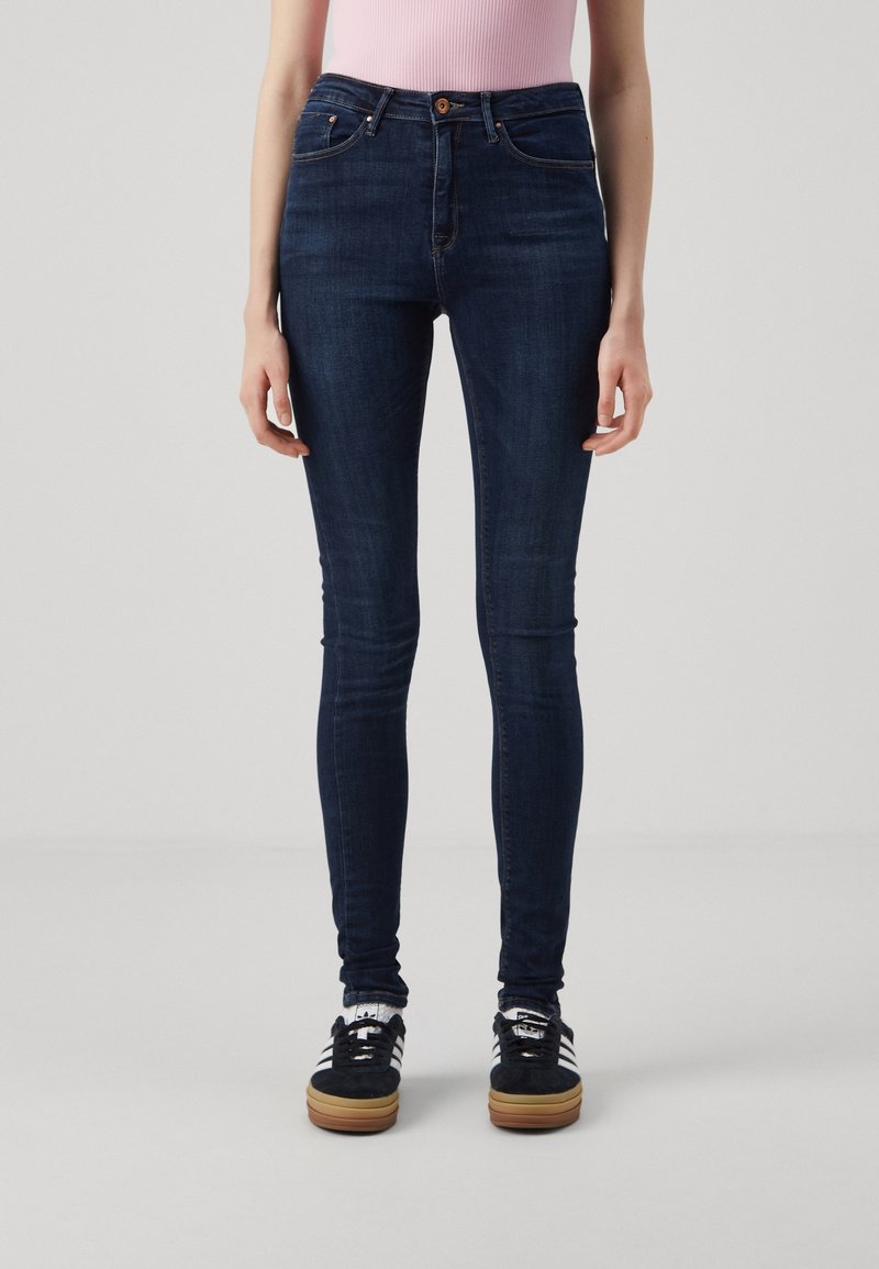 Vaqueros skinny de denim en azul oscuro, con cierre de botón y diseño de cinco bolsillos. La tela tiene una textura suave.