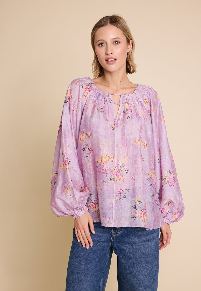 Bluse med blomsterdesign i lys lilla med ballongsiefer, samlet halsutringning og delvis åpning foran. Stoffet har et delikat blomstermønster.