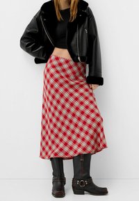 Czerwona długa spódnica w kratę w białe i szare wzory, zestawiona z czarną kurtką z imitacji skóry o krótkim kroju oraz czarnymi botkami z klamrami.