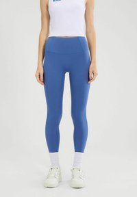 Blaue Leggings mit hoher Taille aus elastischem Material mit glatter Textur. Verfügt über kontrastierende Nähte und eine enganliegende Passform.