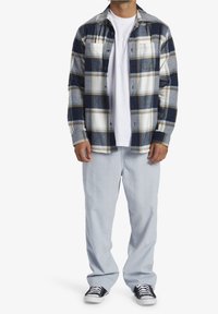 Rutig flanellskjorta i marinblått, grått och krämfärgat. Har två bröstfickor och knappar. Kombinationen med ljusblå jeans och svarta sneakers.