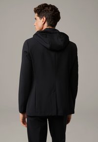 Czarna kurtka z kapturem o eleganckim designie, dopasowanym kształcie i gładkiej fakturze. Ma bezszwowy wygląd i subtelne detale przeszyć.