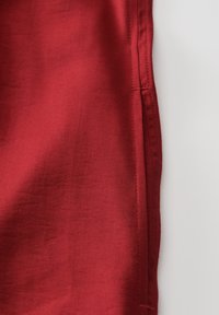 Roter Stoff mit einer glatten Textur, geraden Kanten und sichtbaren Stichen entlang der Nähte.