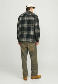 Sort og hvid ternet flannel skjorte med lange ærmer, rygpanel og krave med knappelukning, parret med olivengrønne, afslappede bukser og brune støvler.