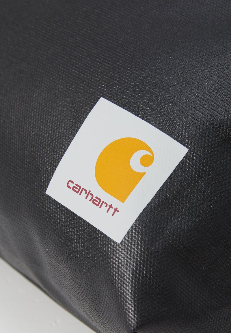 Tissu noir texturé avec un logo Carhartt. Le logo présente un fond blanc et un semicercle orange avec une courbure et le texte "carhartt".