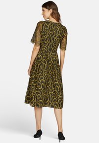 Schwarzes und goldenes gemusterteres Kleid mit kurzen Spitzensäumen, tailliertem Oberteil und schwingendem Rock. Der Stoff weist schwirrlisierende Designs und Texturen auf.