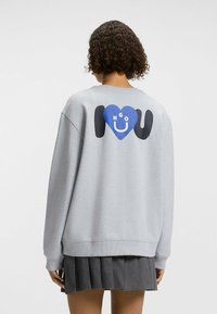 Grijze sweatshirt met een grote graphic op de achterkant, met een blauwe hartvorm en de tekst "HGO U". Casual pasvorm met een geribde zoom.