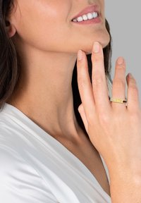 Gold- und Silberring mit einem strukturierten Band an einer Hand, getragen von einer Person mit heller Haut. Der Hintergrund ist neutral und unauffällig.