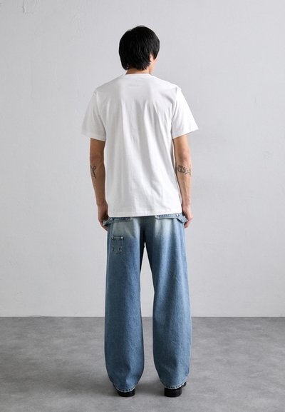 Hvid bomulds-T-shirt kombineret med løstsiddende, lyseblå denim jeans med en falmet gradient og en detalje på baglommen.