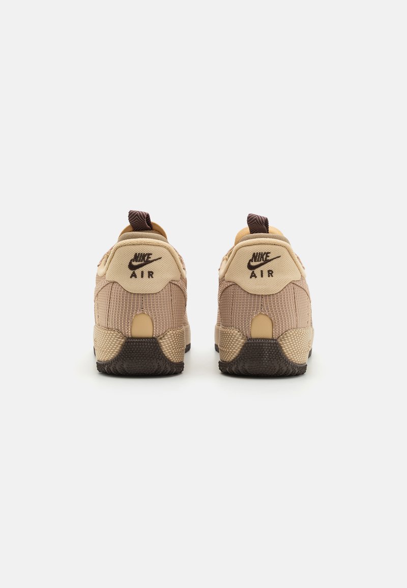 Sneakers Nike Air beige con tessuto testurizzato, accenti marrone scuro e suola in gomma. Presentano il logo sul retro e un collare imbottito.