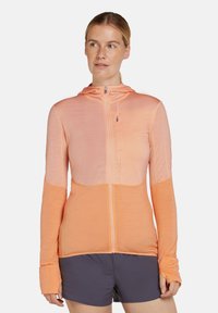 Chaqueta ligera con capucha en tonos degradados de durazno y coral. Presenta un cierre completo, mangas largas y una tela texturizada con sutiles líneas de acanalado.