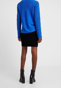 Modrý pletený svetr s žebrovanou texturou na horní polovině, kombinovaný s černou úzkou sukní s vodorovnými pruhy a černými kotníkovými botami.