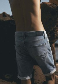 Shorts de mezclilla en azul claro, con dobladillos enrollados, dos bolsillos traseros y una etiqueta tejida en la cinturilla trasera.