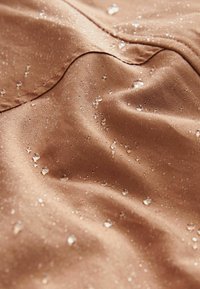 Water droplets beading on smooth brown waterproof fabric with visible seams and slight wrinkles.