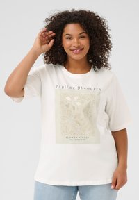 T-shirt en coton blanc à manches courtes, avec un motif floral beige et du texte sur le devant. Le tissu semble lisse et léger.