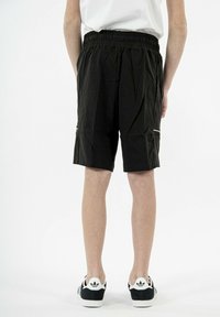 Pantalones cortos negros con una cinturilla elástica, bolsillos laterales y costuras de acento en blanco, combinados con zapatillas blancas y negras.
