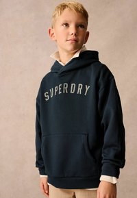 Sudadera con capucha de color azul marino con "SUPERDRY" bordado en gris. Cuenta con un bolsillo frontal y puños y dobladillo acanalados. Material de algodón suave.