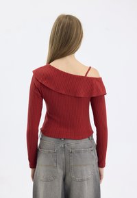 Red ribbed long-sleeve top with off-the-shoulder design and wide collar. Paired with high-waisted grey denim pants featuring back pockets.