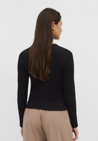 Sort ribbet langærmet top med en tætsiddende design og rund halsudskæring, parret med beige, lette, høj taljede bukser.