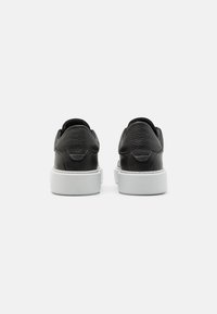 Zapatillas de cuero negro con un acabado texturizado, suela de goma blanca y forma redondeada; cuentan con un cuello acolchado y un diseño minimalista.