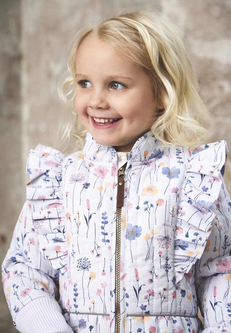 Veste rembourrée fleurie en blanc, avec des épaules froncées, une fermeture éclair sur le devant et de délicats motifs de fleurs roses, bleues et jaunes.
