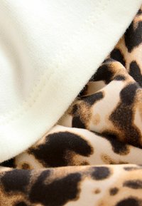 Un tissu en coton couleur crème superposé avec un tissu beige à imprimé léopard dans des tons marron et noir, montrant des détails de texture et de couture.